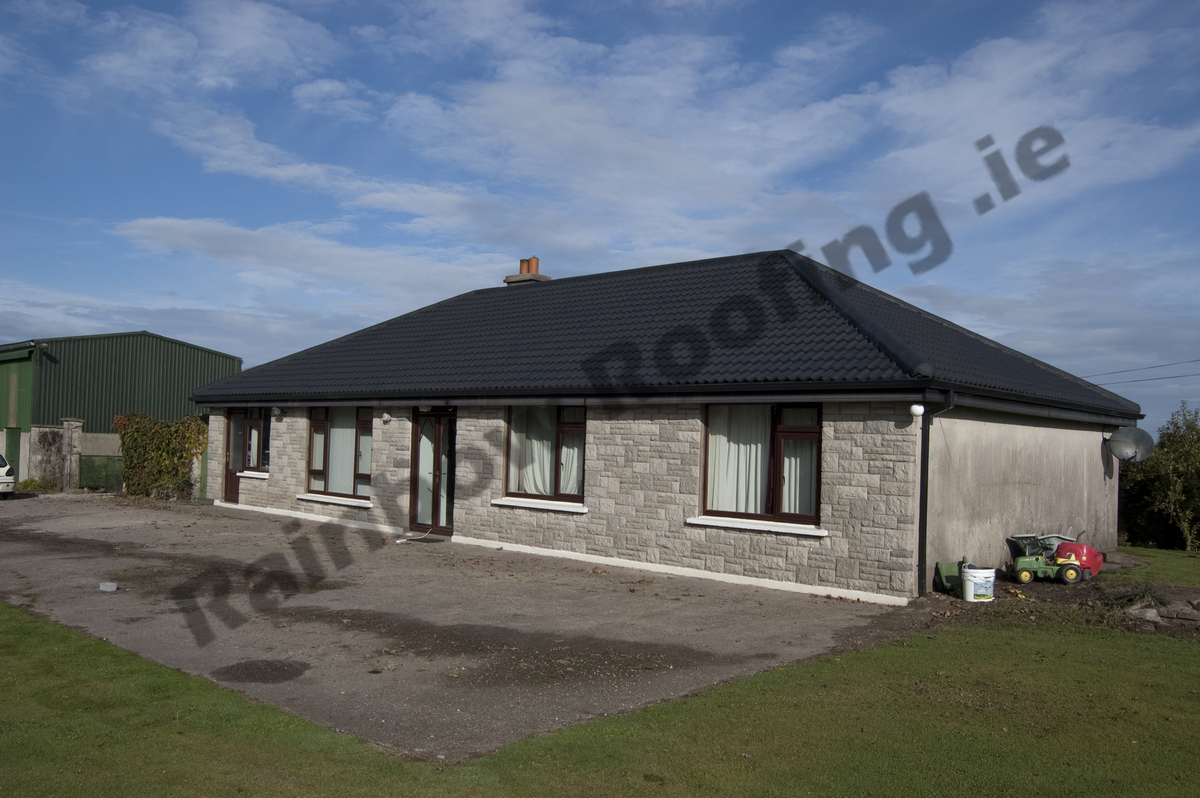 Small stone clad bungalow house with newly spray painted dark blue roof tiles.