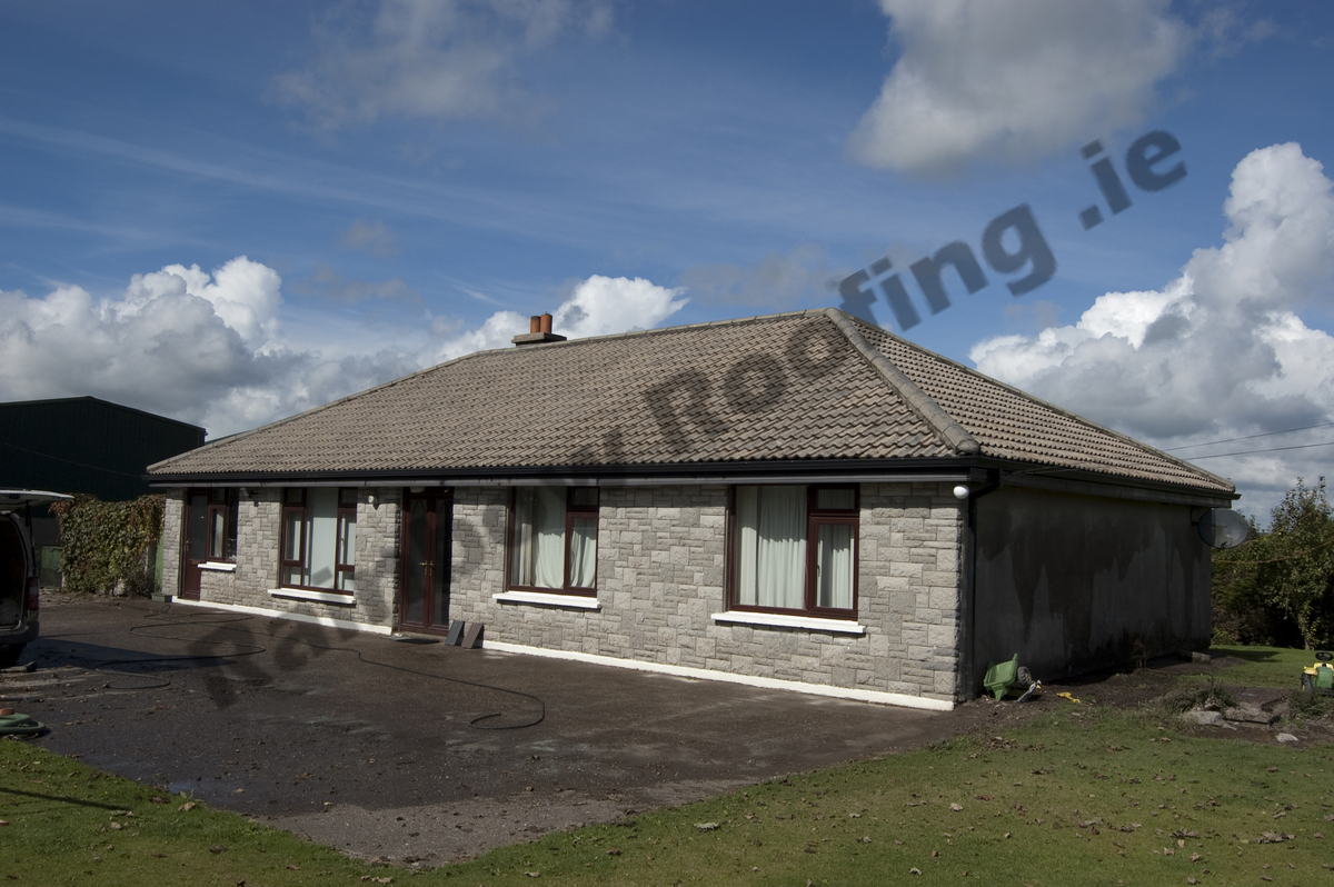 Small stone clad bungalow house with faded roof tiles.